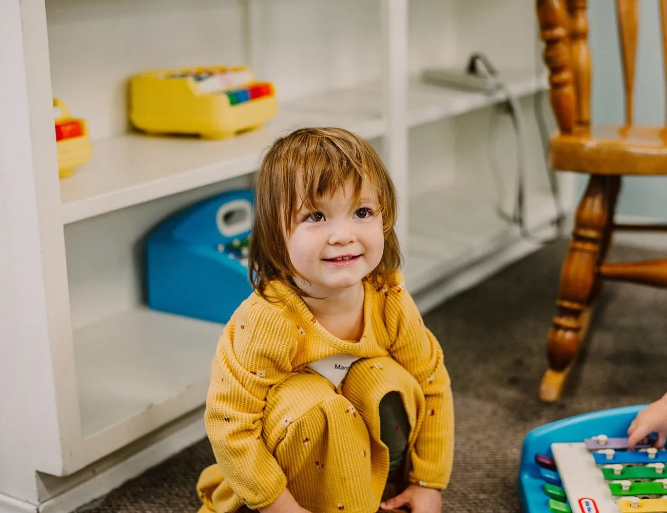 A smiling toddler looking up while playing in the nursery