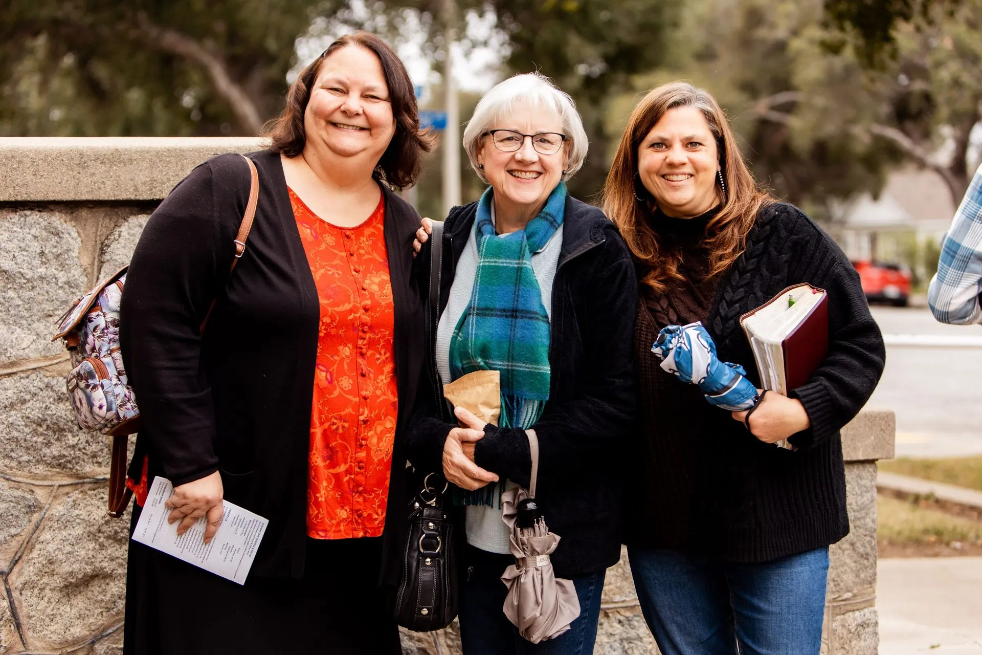 Three women smiling together outside the church, holding Bibles